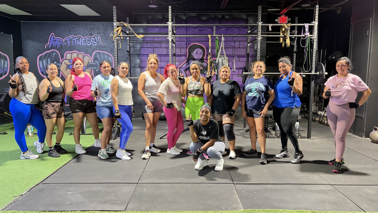 Miembros de AMP juntos frente al mural de AMP Fitness