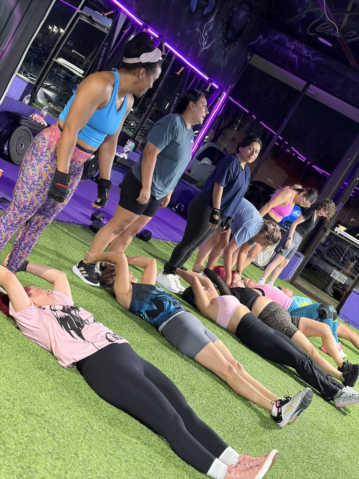 Miembros haciendo un ejercicio en pareja con coach bajo las luces moradas de AMP Fitness Studio
